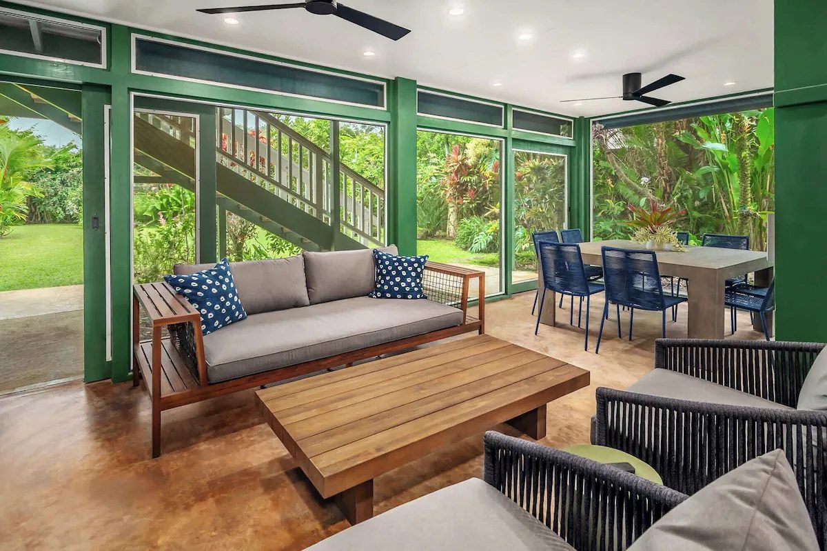 Screened lower lanai with a teak sofa, low table and an outdoor dining table opening to the lawn.