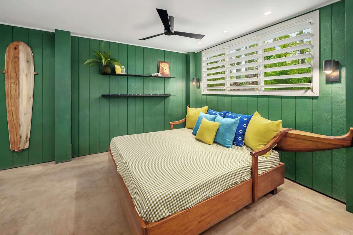 Green board-and-batten room downstairs with a daybed, surfboard and louvered windows.
